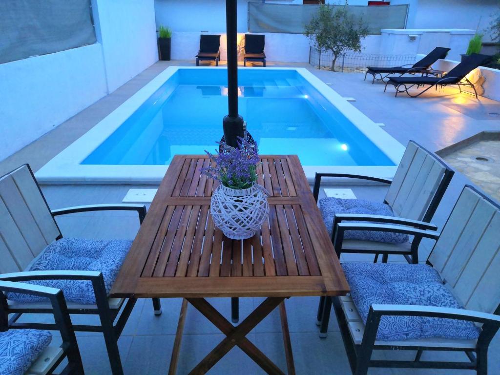 una mesa de madera con sillas junto a la piscina en Cypress Tree Holiday Apartments, en Privlaka