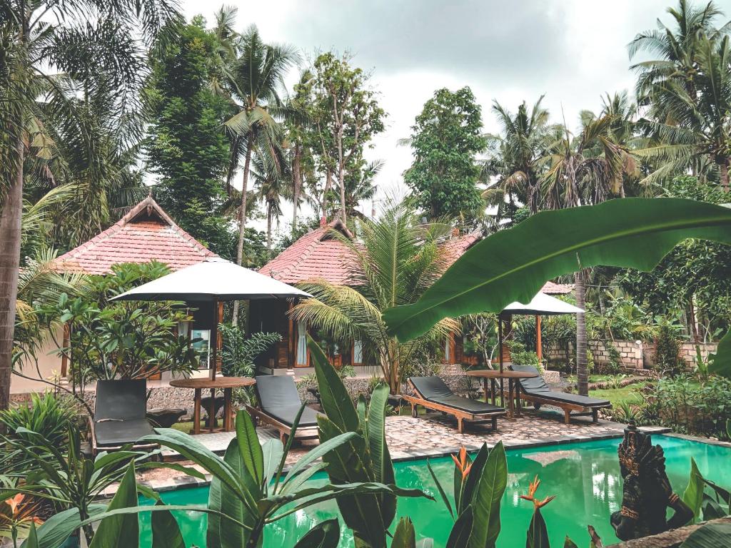 a resort with a pool and tables and umbrellas at The Valley Green Cottage in Nusa Penida