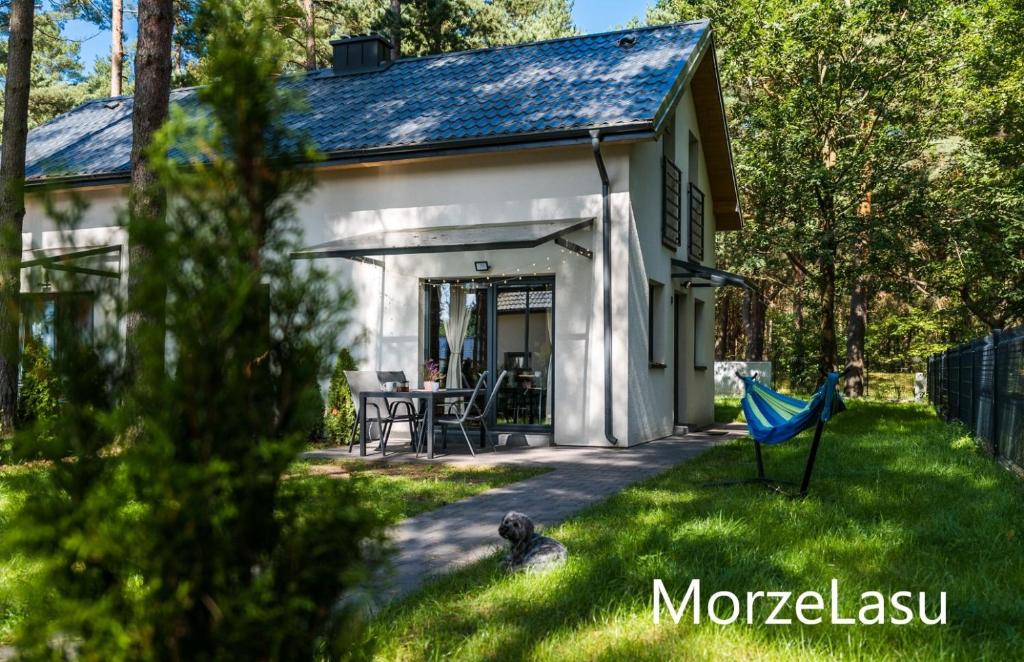 une petite maison blanche avec un hamac bleu dans la cour dans l'établissement Domek MorzeLasu Ostrowo Jastrzębia Góra, à Ostrowo