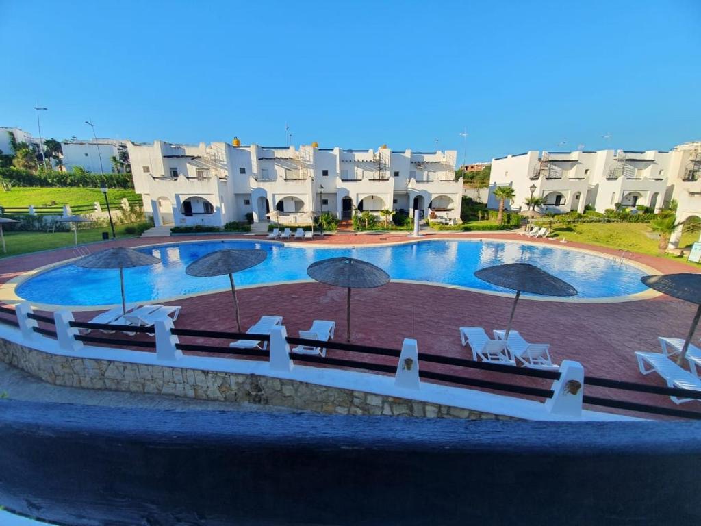 a swimming pool with chairs and umbrellas in front of some buildings at La Vida Villa Alcudia Smir Fnideq, Holiday Homes in Tetouan