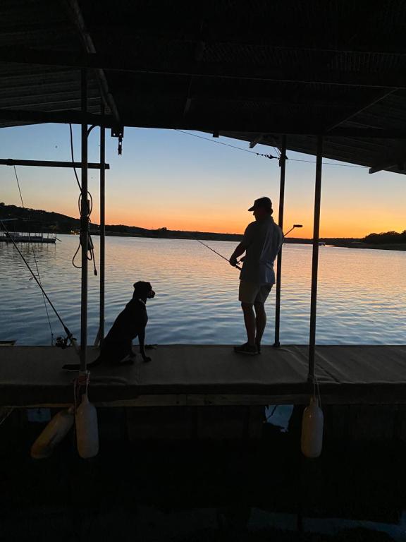 Ein Mann steht auf einem Dock mit einem Hund auf einem Boot. in der Unterkunft Lakefront Oasis on Lake Travis! in Spicewood