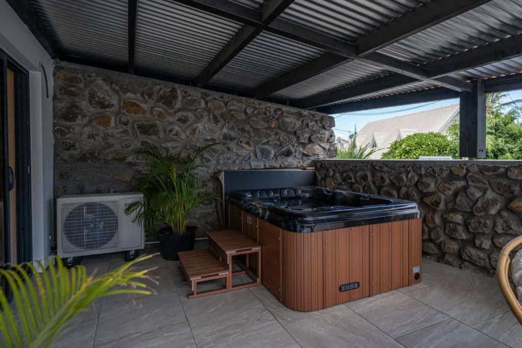 a patio with an outdoor kitchen with a stone wall at Le Temps d'Aime in Le Bois de Nèfles
