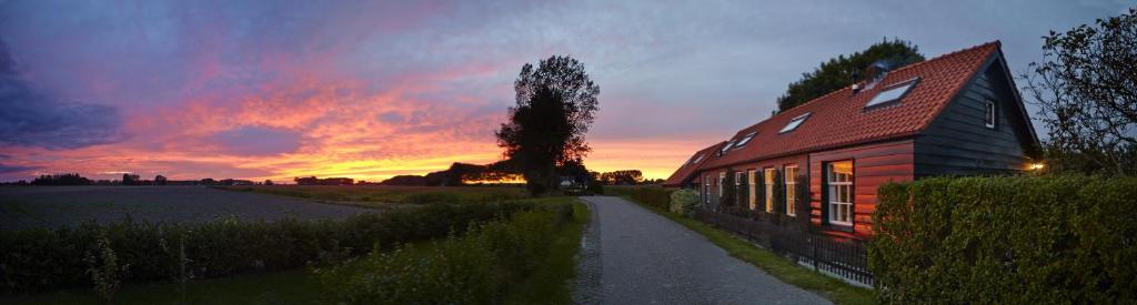 a red house with a sunset in the background at Polderhuis voor 8-10 personen aan zee in Nieuwvliet