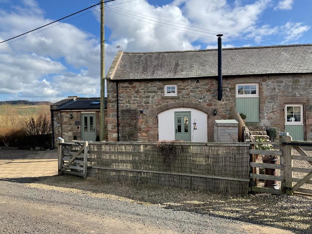 una casa de piedra con una valla delante de ella en Hetton Byre en Lowick