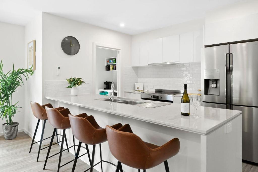 a white kitchen with a counter with chairs and a refrigerator at Chatleys in Aireys Inlet