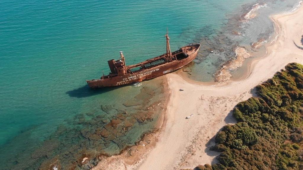 an old boat in the water next to a beach at The Olive Yard in Gythio