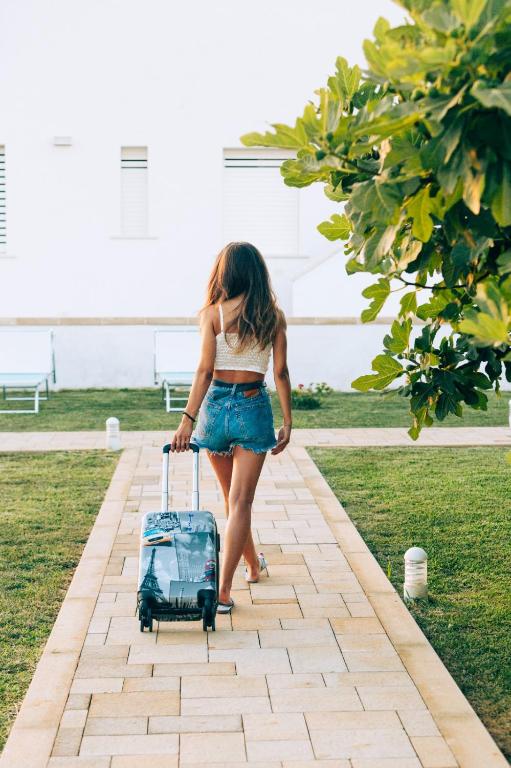a woman walking with a suitcase on a sidewalk at B&B Domus Terra Mare in Torre San Giovanni Ugento