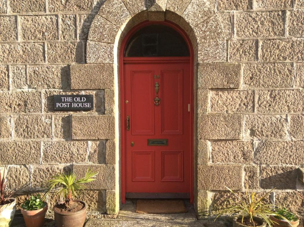 a red door in a stone wall with a sign at The Old Post House B&B in St. Just