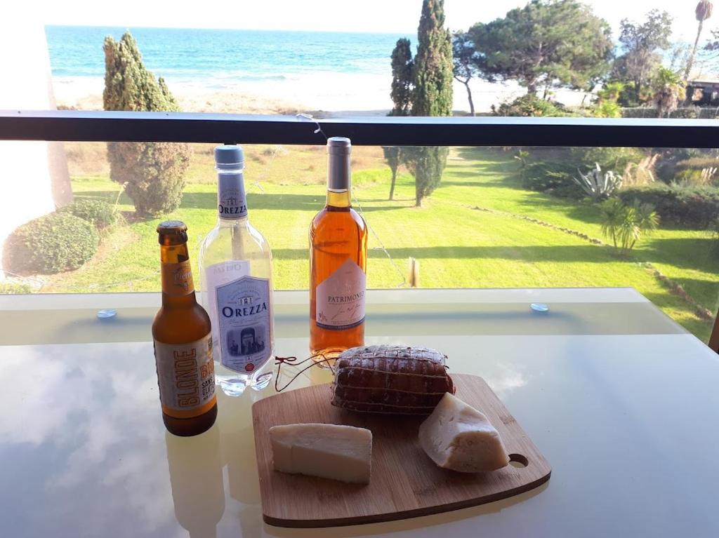 - deux bouteilles de vin et de fromage sur une table avec une fenêtre dans l'établissement Résidence Les Marines de Moriani pieds dans l'eau duplex avec terrasses vue mer, 4-8 pers, à San-Nicolao