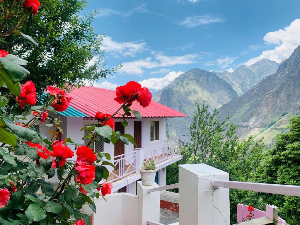 a white house with red flowers and mountains in the background at Ramneek Homestay in Joshīmath