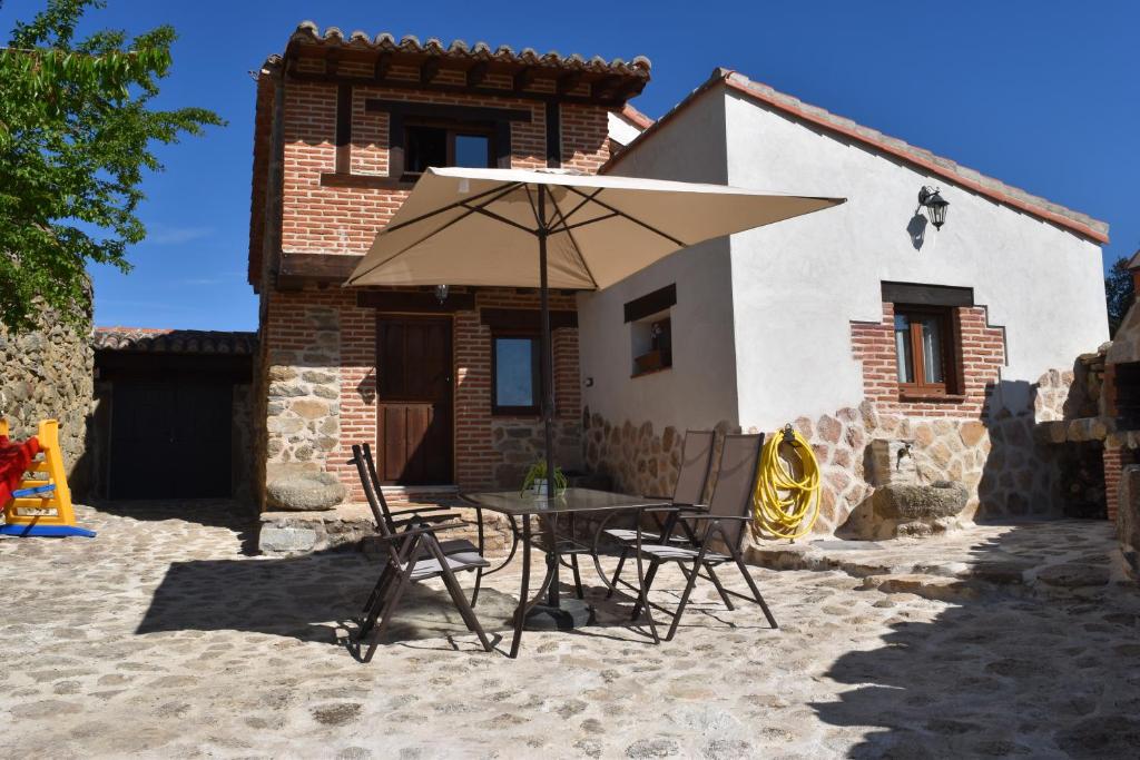 - une table et des chaises avec un parasol en face d'une maison dans l'établissement Casa Rural El Balcón de Piedrahíta, à Navahermosa de Corneja