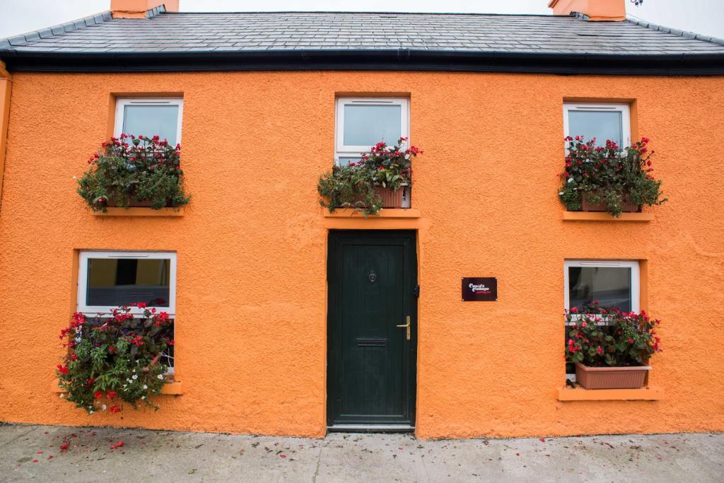 una casa naranja con flores en las ventanas y una puerta en Charming 2-Bed House in West Cork Cupid's Cottage en Kealkill