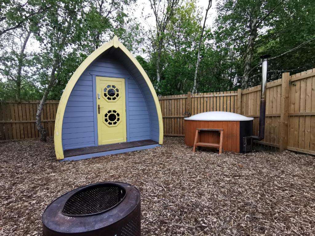 a blue and yellow dog house next to a wooden fence at Cosy Forest Pod with Wood Fired Hot Tub & Fire Pit in Hambleton