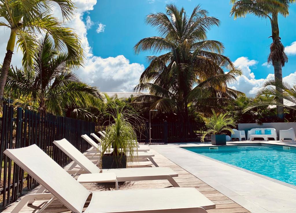 - une piscine avec des chaises longues blanches et des palmiers dans l'établissement Résidence de tourisme Domaine Saint-François, à Saint-François