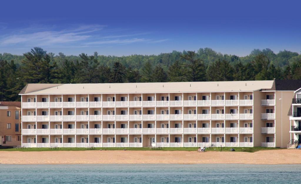 a large white building next to a body of water at Mackinaw Beach and Bay Inn & Suites in Mackinaw City