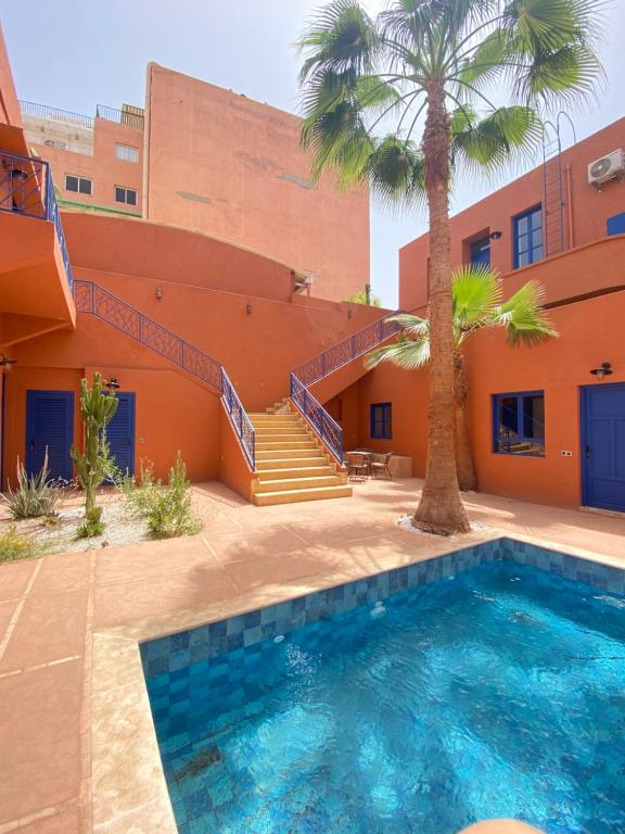 a swimming pool in front of a building with a palm tree at Comfy Colonial Apartments in Marrakesh