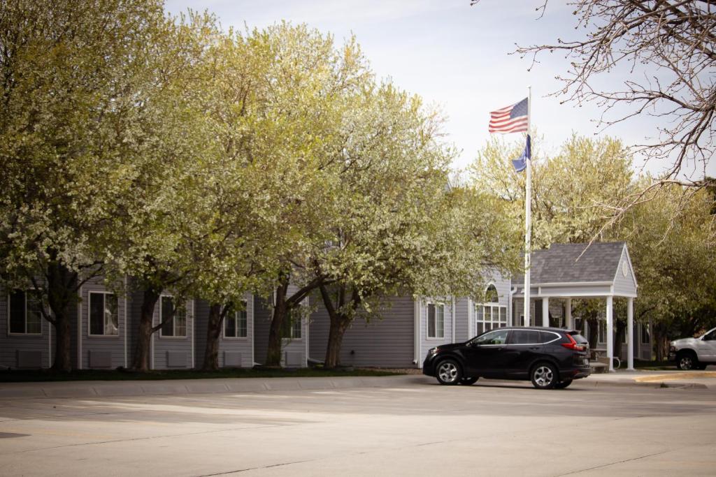 une voiture noire garée devant une maison arborant un drapeau américain dans l'établissement Monument Inn & Suites, à Gering