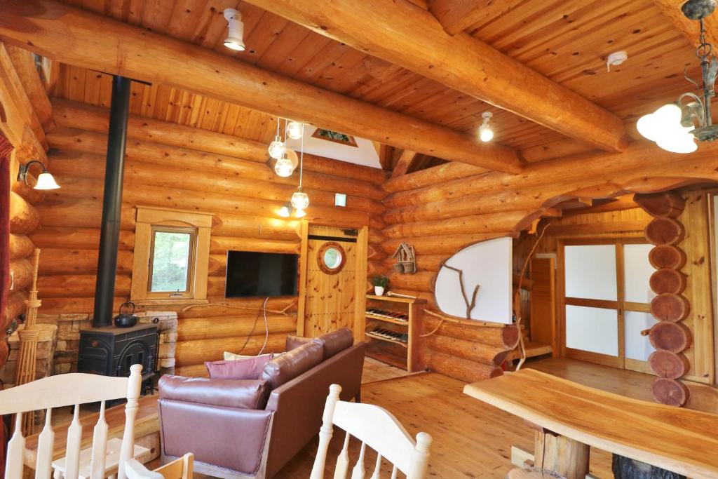 Cabaña de madera con sala de estar con sofá y fogones en ログキャビン伊豆高原 en Futo