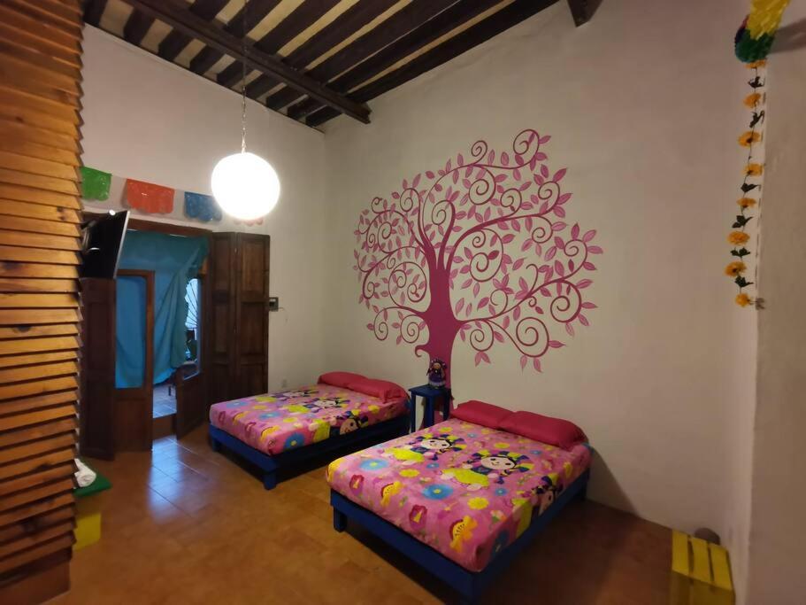 a room with two beds and a tree on the wall at Lele Panchito y Lavanda Juntos en el Centro in Querétaro