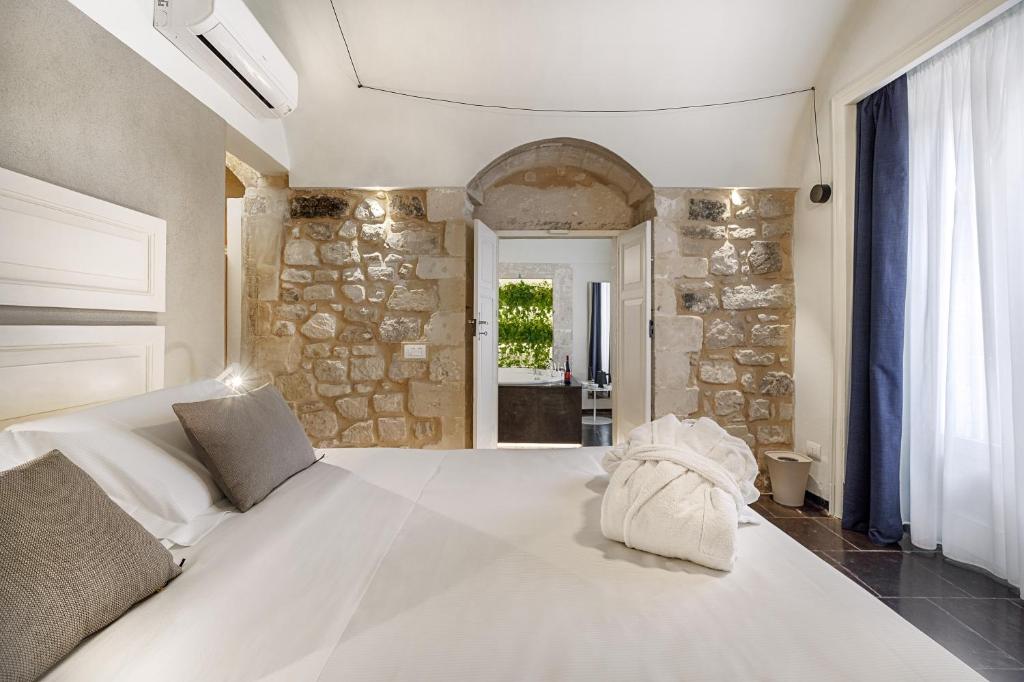 a bedroom with a large white bed and a stone wall at Iblaresort Boutique Hotel in Ragusa