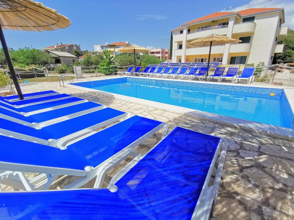 a swimming pool with blue chairs and an umbrella at Apartments CVITA Holiday in Rogoznica