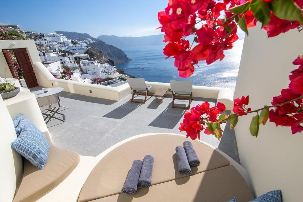 einen Balkon mit einem Tisch und roten Blumen in der Unterkunft Elegant Santorini Villa Villa Spyros Villa Demi Private Hot Tub Air Conditioning 2 Bedroom in Oia