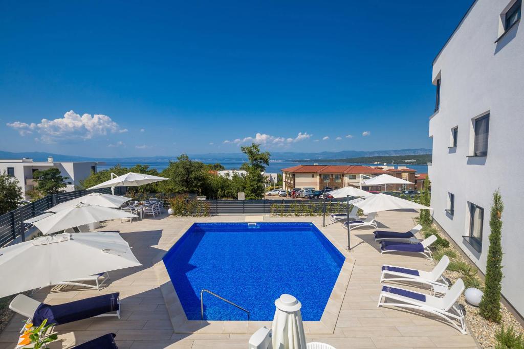 a swimming pool with chairs and umbrellas next to a building at Villa Poseidon Rova by EL-PI TOURS in Malinska