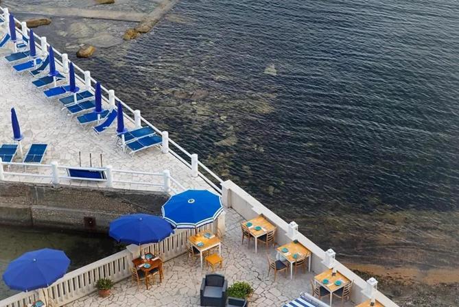 un grupo de mesas y sillas con sombrillas azules y agua en Hotel Le Najadi, en Santa Marinella