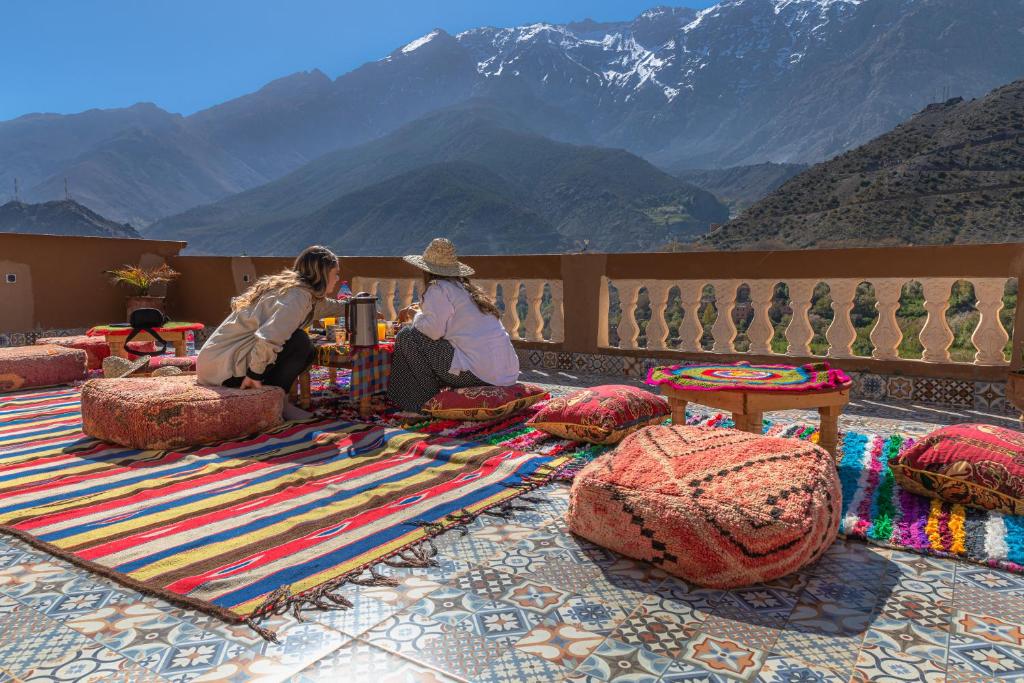 two people sitting on a rug with mountains in the background at Amazigh Family Riad in Imlil