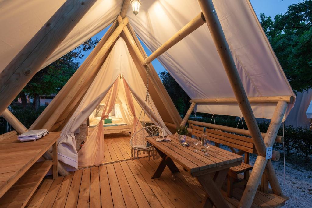 Tienda con terraza de madera con mesa de madera y bancos en Eco glamping- FKK Nudist Camping Solaris en Poreč