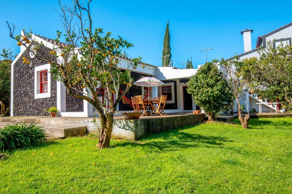 ein Haus mit einem Hof mit einem Tisch und einem Sonnenschirm in der Unterkunft Quinta dos Reis in Biscoitos