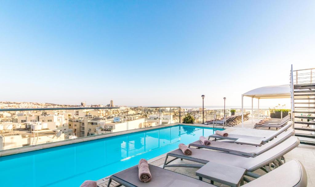 a pool with lounge chairs and a view of the city at AX The Victoria Hotel in Sliema