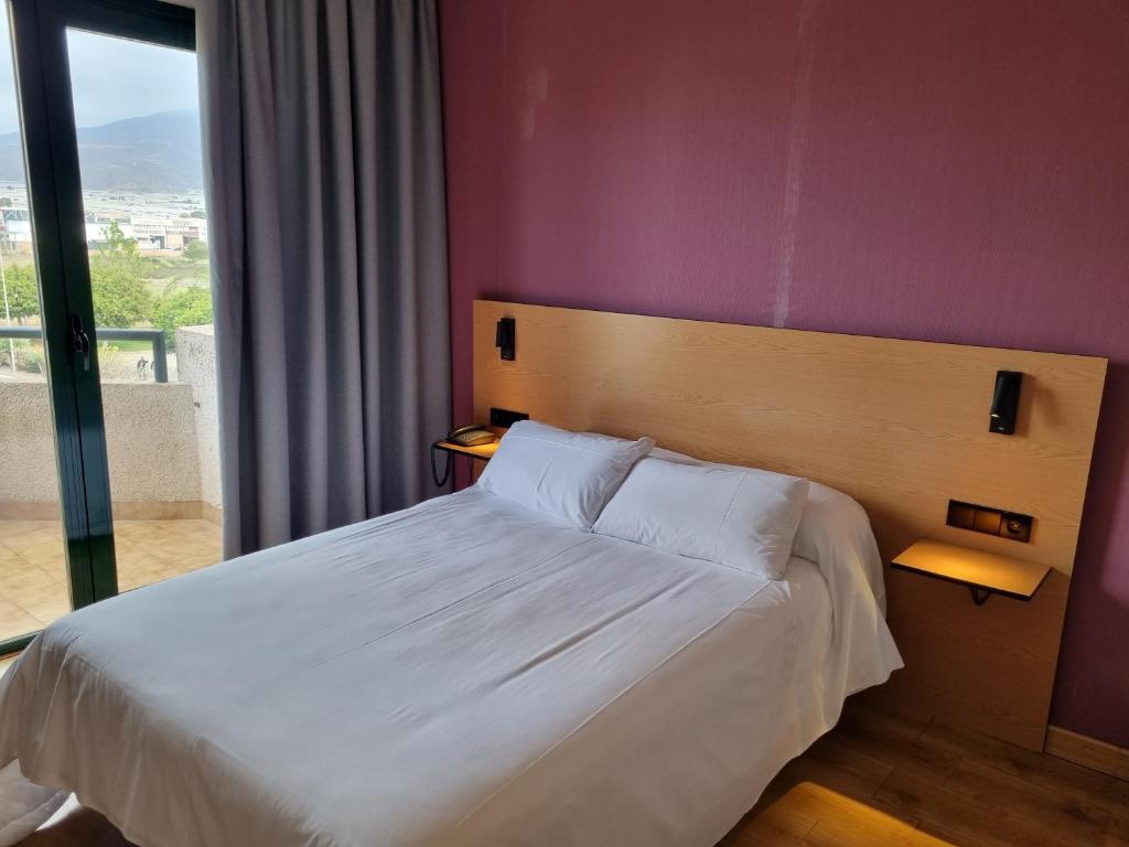 Ejido Hotel في إل خيدو: غرفة نوم بسرير ابيض وبجدار ارجواني