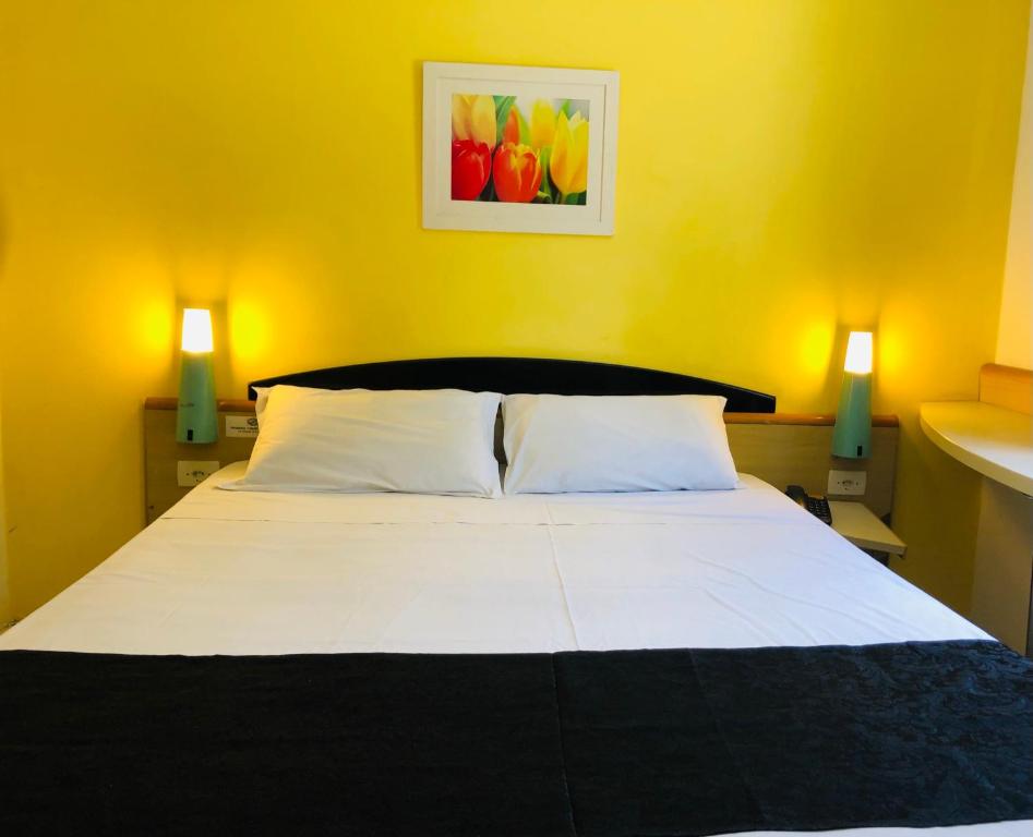 a bedroom with a white bed with a yellow wall at Hotel Blumenau Centro in Curitiba