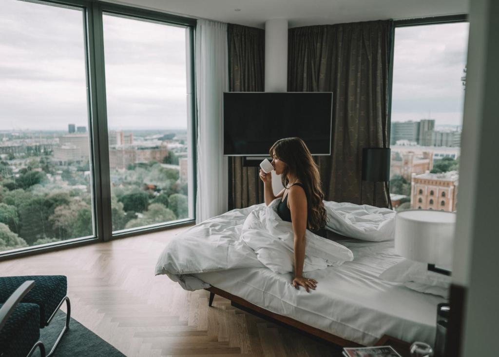 a woman sitting on a bed in a hotel room at Andaz Vienna Am Belvedere - a concept by Hyatt in Vienna