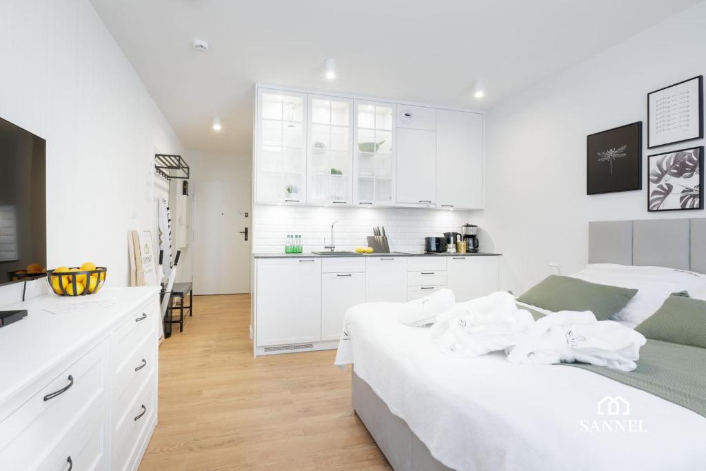 a white bedroom with a large bed and a kitchen at Apartament Baltic Amber z dostępem do basenów,strefy saun, jacuzzi przez cały rok- Pinea Apartments Pobierowo-SANNEL Apartments for rent in Pobierowo