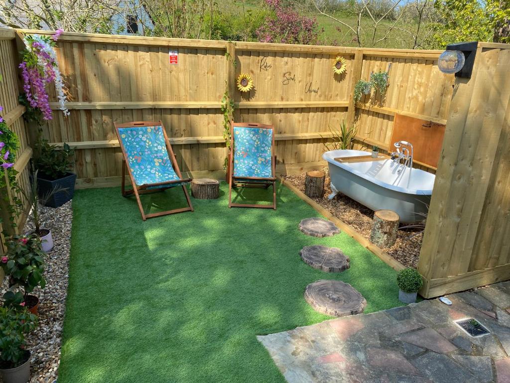 Cosy dog friendly lodge with an outdoor bath on the Isle of Wight في Whitwell: كرسيين وحوض استحمام في حديقة خلفية