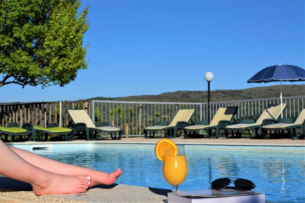 a woman sitting next to a swimming pool with a drink at Hotel Vista Bela do Gerês in Outeiro