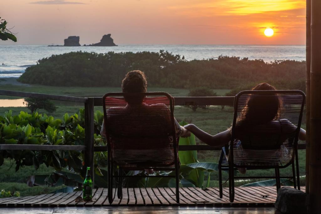 twee mensen zittend in stoelen op een veranda kijkend naar de zonsondergang bij Vistamar Guest House in Ayampe