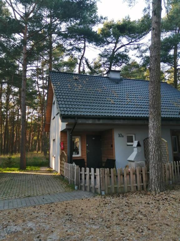 a small white house with a fence and a tree at Domek na Leśnej in Pogorzelica