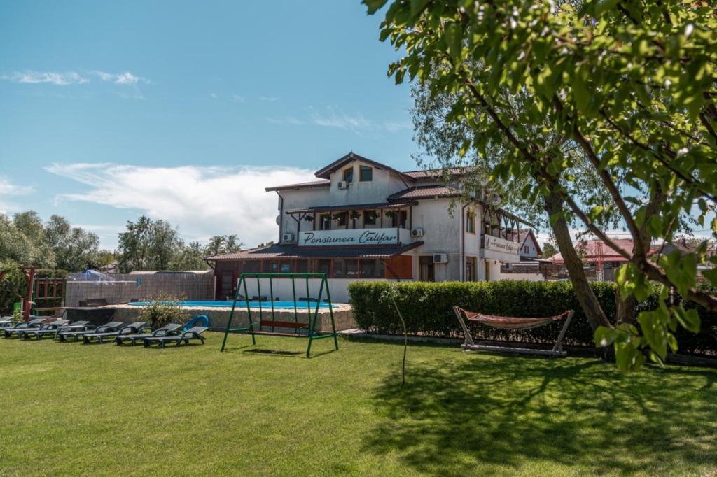 a building with a pool and chairs in a yard at Pensiunea Califar in Dunavăţu de Jos