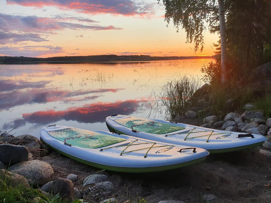drei Boote, die bei Sonnenuntergang am Ufer eines Sees sitzen in der Unterkunft Hidden Island Laukanharju Glamping in Savonlinna
