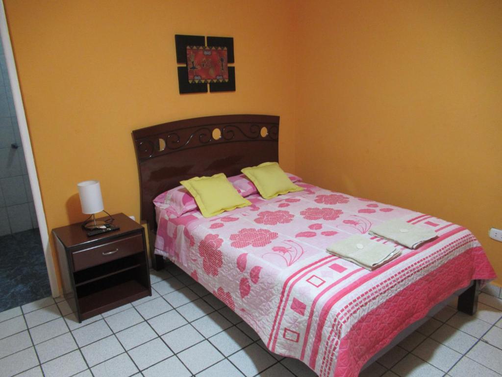 um quarto com uma cama e uma mesa de cabeceira com um cobertor rosa e amarelo em Kurmi Hostel Lima Airport em Lima