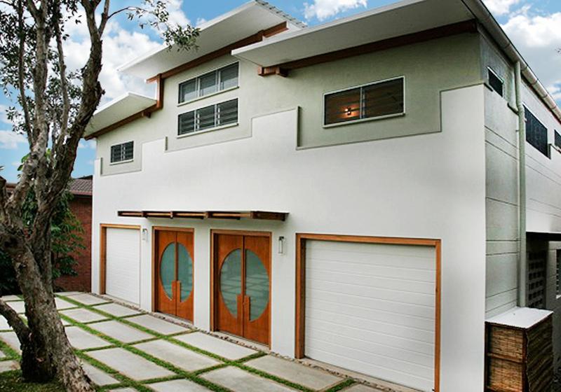 una casa blanca con dos puertas de garaje y un árbol en THE BEACH HAVENS en Emerald Beach