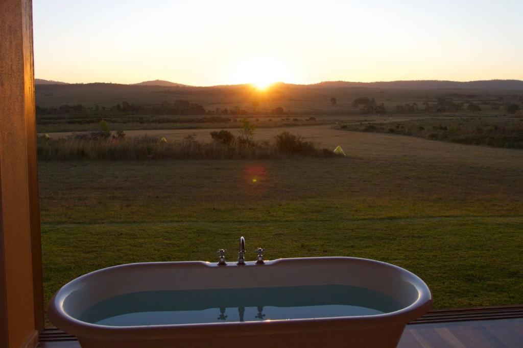eine Badewanne vor einem Fenster mit Blick auf den Sonnenuntergang in der Unterkunft Toumbaal Plains - Exquisite architecturally designed home in Brooms Head