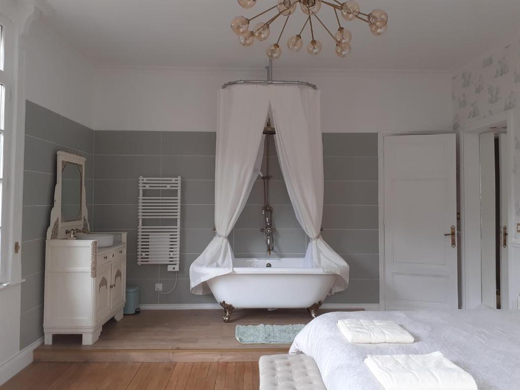 un bagno con vasca, un letto e un lampadario a braccio di Manoir de Camblain a Camblain-lʼAbbé