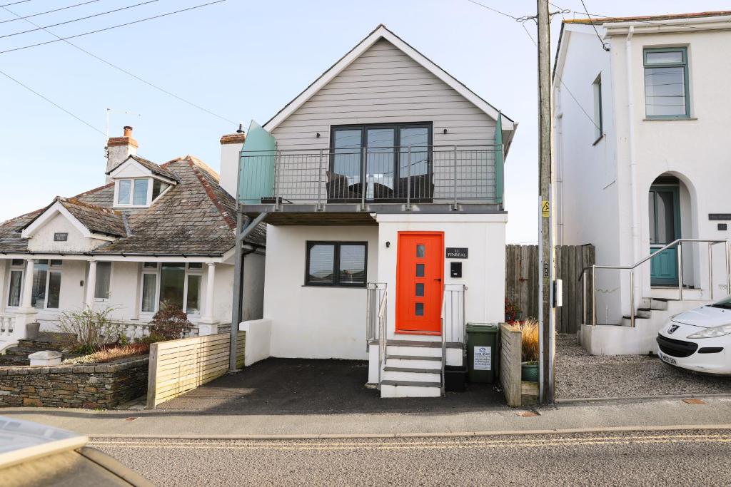 a white house with an orange door on a street at Penreal, Port Isaac Bay Holidays in Port Isaac