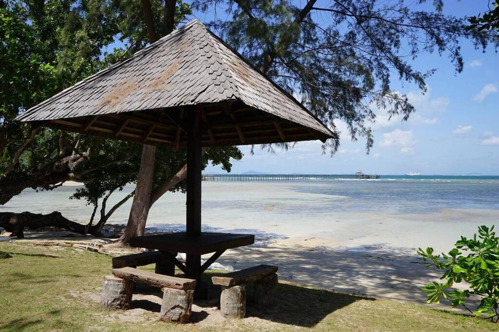 eine Bank und ein Sonnenschirm am Strand mit Wasser in der Unterkunft Elysia Nongsa 24 Batam Luxury Villa in Nongsa