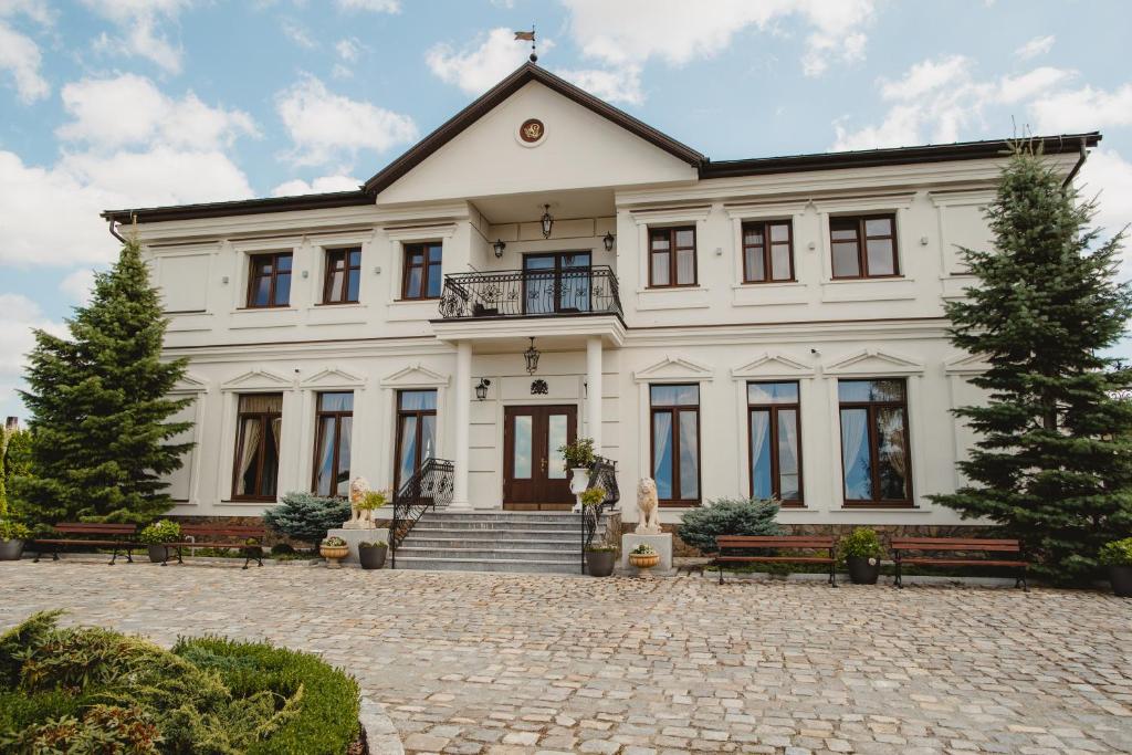 uma grande casa branca com bancos à sua frente em Pałac Uniejów em Uniejow