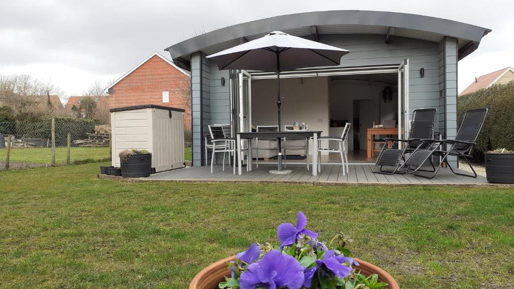 eine Terrasse mit einem Sonnenschirm und einem Tisch mit lila Blumen in der Unterkunft The Annexe, Cornfields in Elmswell